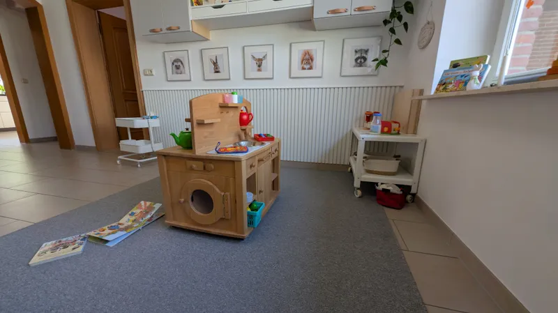 Gemütlicher Spielraum mit Kinderküche, Büchern und altersgerechten Spielmaterialien in warmer, einladender Atmosphäre