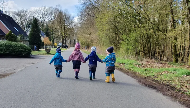 Vier Kinder halten Hände bei einem Spaziergang in die Natur – gemeinsame Ausflüge fördern soziale Bindung