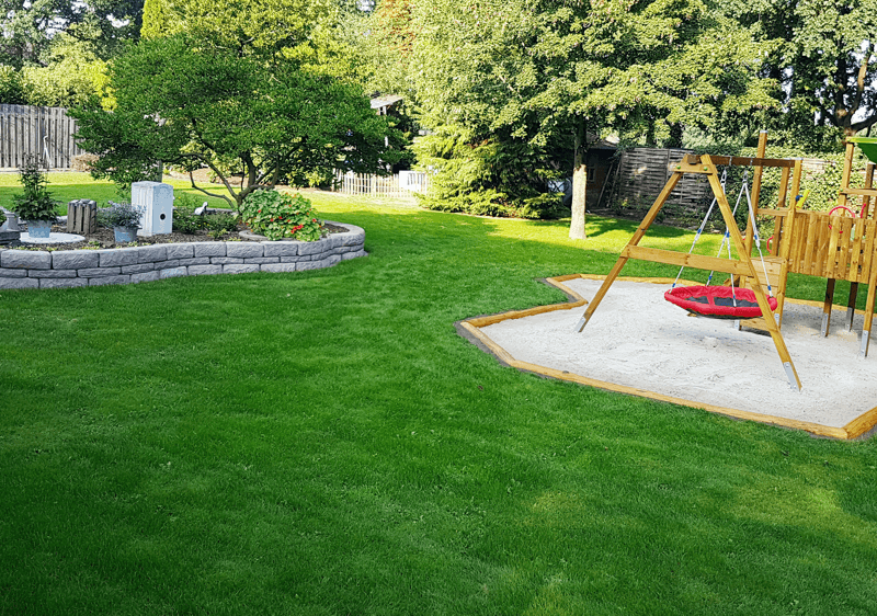 Großer Garten mit Sitzbereich, Sandkasten und natürlichen Spielmöglichkeiten für Kinder