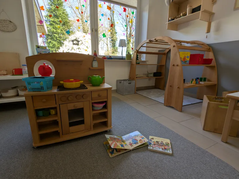 Kinderfreundlicher Spielbereich mit Holzküche und Bilderbüchern auf dem Teppich für spielerische Sprachförderung im Alltag